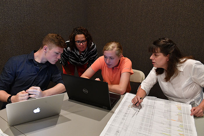 Two students and two adults look at a laptop computer