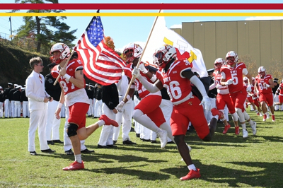 NCAA Division 1 VMI football players take to the field carrying the American and VMI flags.