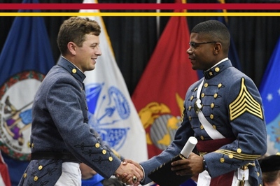 Two graduates shake hands crossing the stage in Cameron Hall during commencement at VMI.