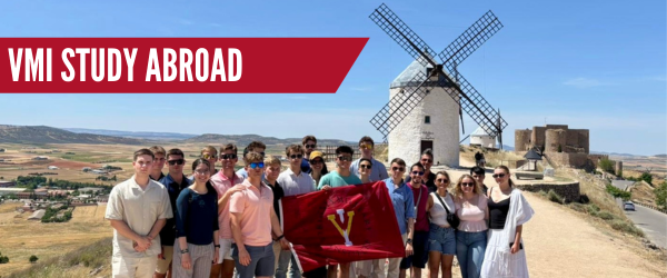Cadets pose in front of a windmill and holding a VMI flag abroad.