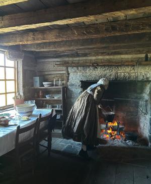 A costumed interpreter tends to the fire in the Bushong Farm Kitchen.