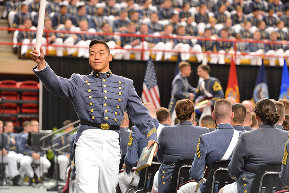 A cadet waves his diploma in the air as he crosses the stage.