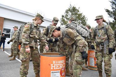 Cadets put canned food into a large orange barrel. 