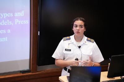 Honors student Gabriele Woodward ’24 stands at a laptop in front of a screen presenting her research at VMI, a military college in Virginia.