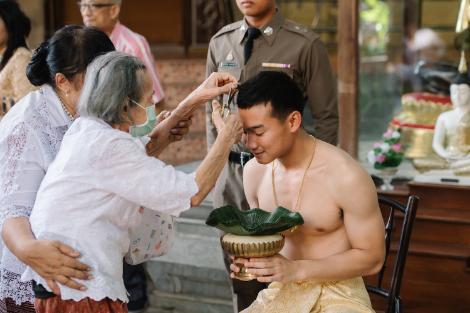 The grandmother of Kanokpon “Gun” Mettasat ’27 clips a lock of his hair during the haircut ritual last June in Thailand.