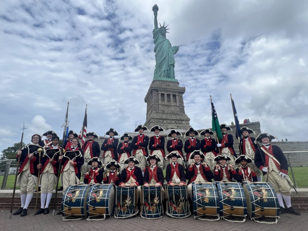 Fife and Drum group photo with instruments in front of the Statue of Liberty.