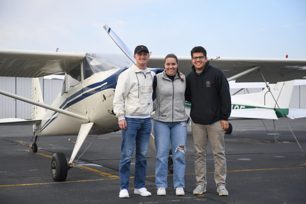 Three VMI Cadets stand in front of a plane on the tar mat, as part of the school's aviation club.