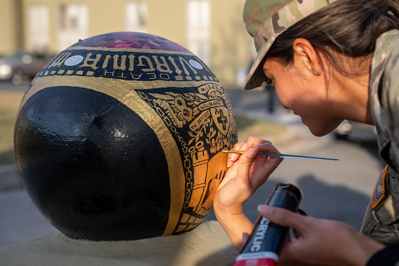 A female student (cadet) at VMI paints this year's ring design onto a cannonball.