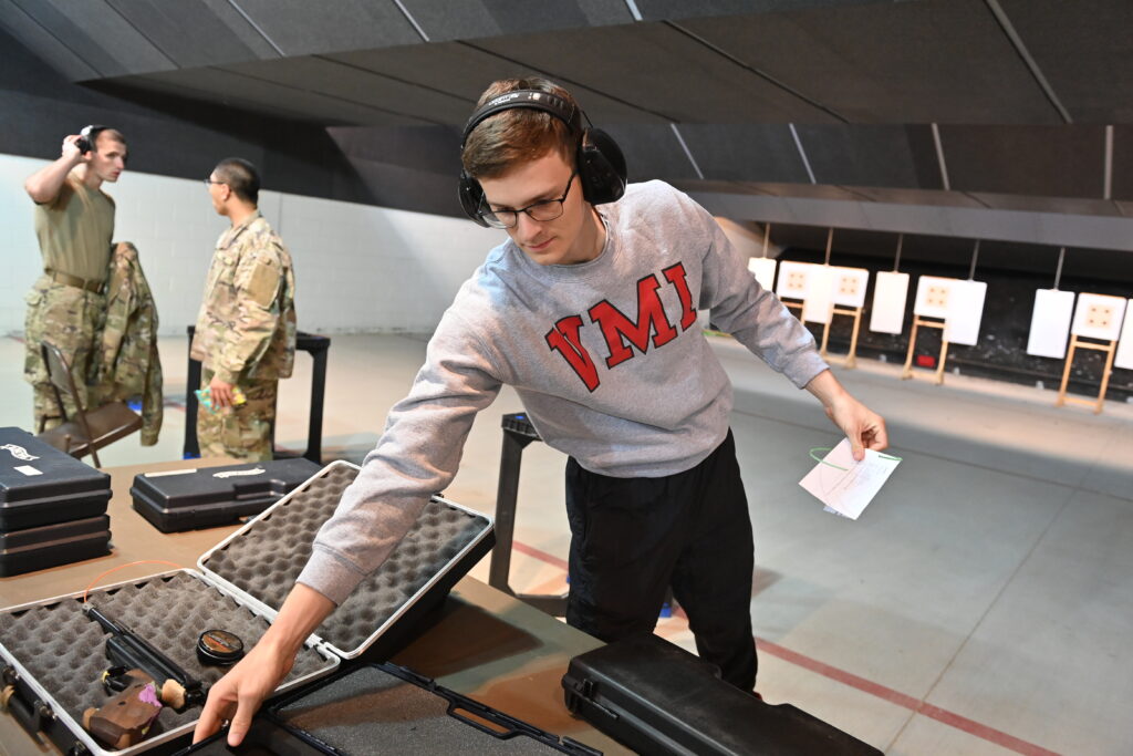 A cadet in the shooting range placing guns back in cases.