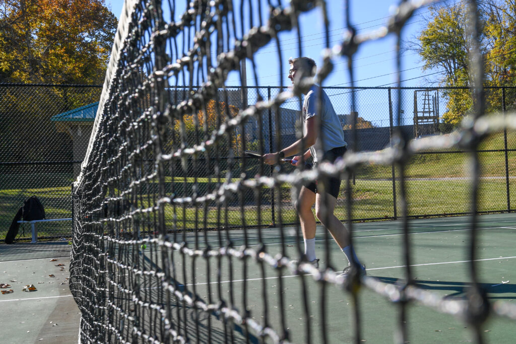 A cadet behind a net on the tennis court.