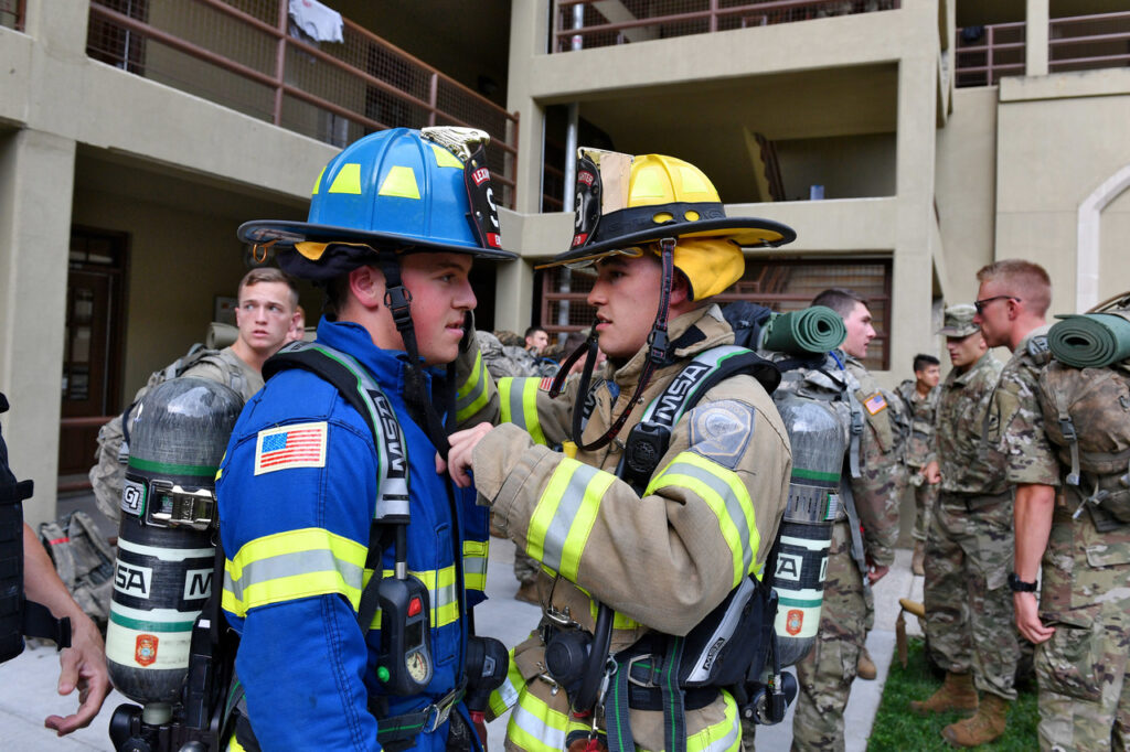 Two cadets gear up in firefighting equipment in barracks.