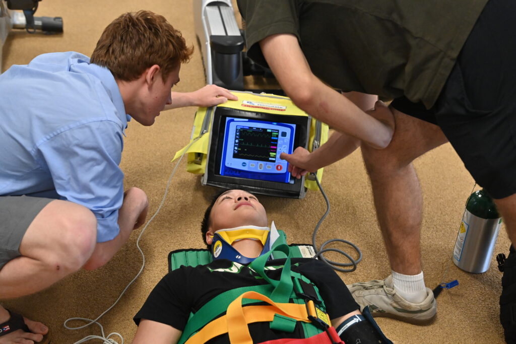 Cadets carry out a scenario-based drill as two monitor the vital signs of a third posing as a patient.