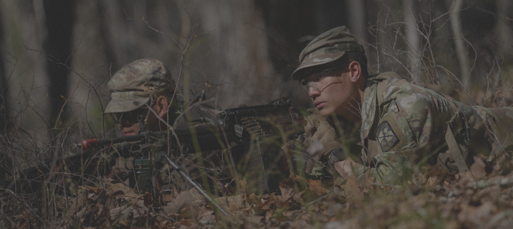 Cadets in a forest, practicing log range fire training, as part of Army ROTC.