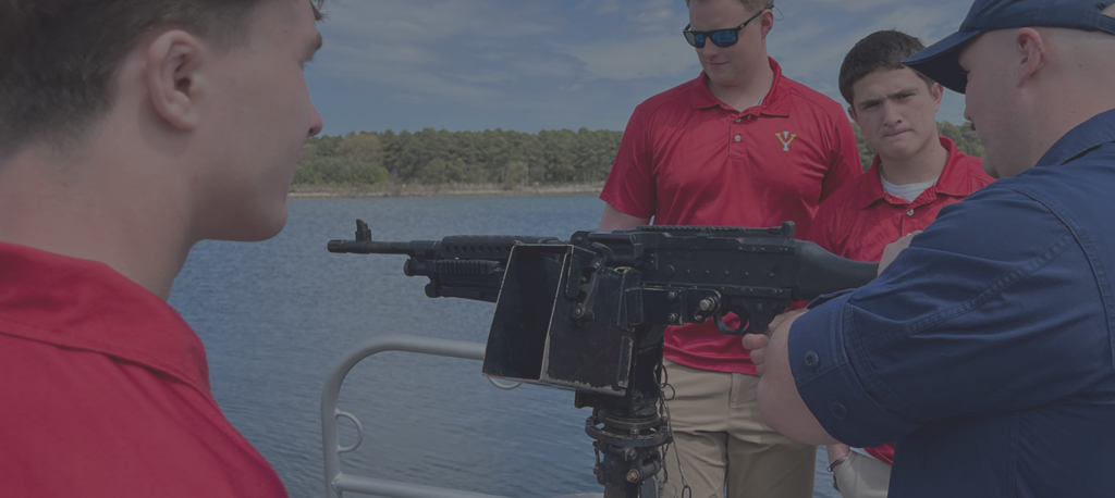 Cadets on a boat, being taught about mounted guns, as part of Coast Guard ROTC.